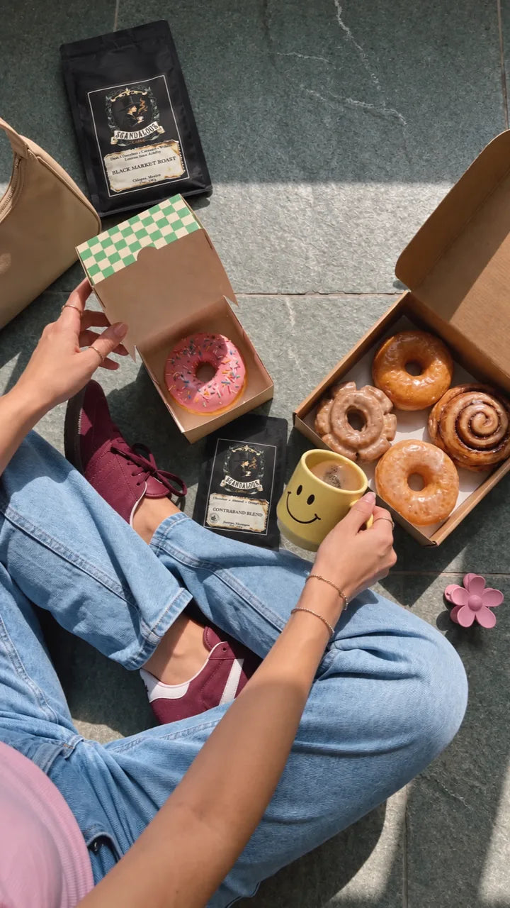 Overhead picnic with doughnuts, a yellow coffee mug, and Black Market Roast and Contraband Blend pouches.