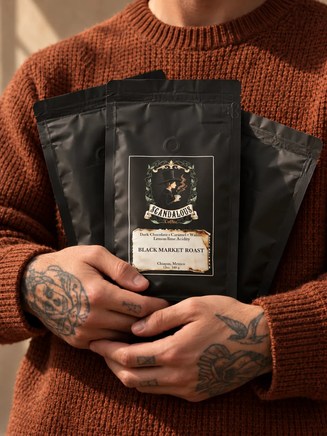Hands holding Scandalous Coffee bags with Black Market Roast in front, rust knit sweater