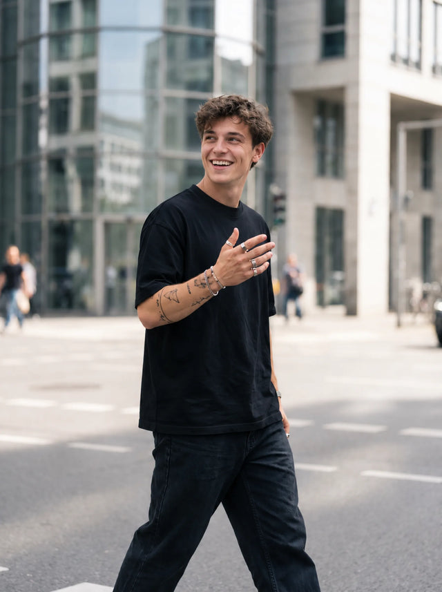 A fictional adult in a plain black outfit walks past glass city buildings with one tattooed hand raised.